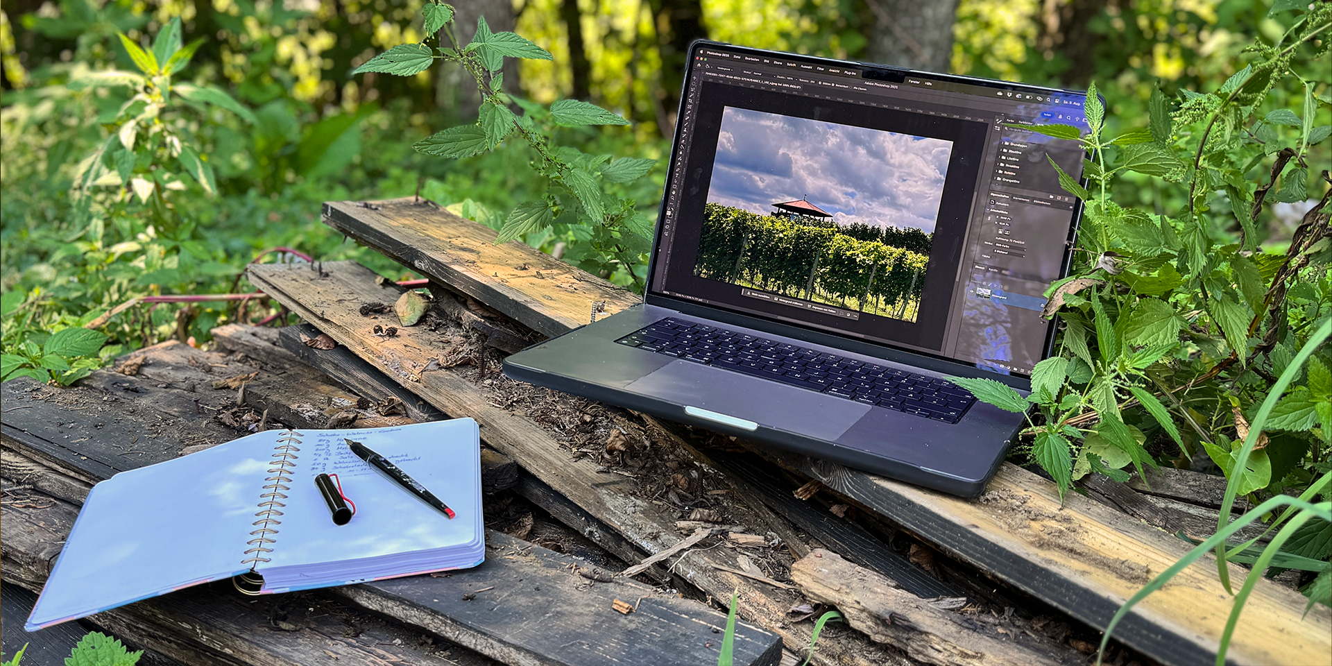 Aufgeschlagenes Notizbuch und Laptop in einer moosigen Wiese mit Baum im Hintergrund.